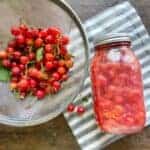 Hollander full of cherries and a jar full of homemade cherry pie filling on a grey and white striped cloth napkin